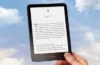 Ruka drží čtečku Amazon Kindle proti modré obloze