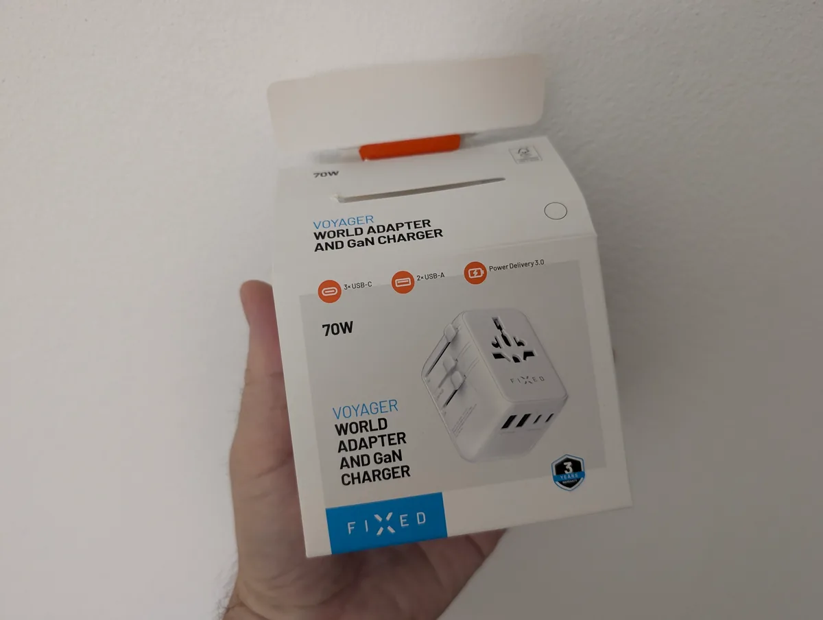 Cestovní adaptér FIXED Voyager 70W nabije z jedné zásuvky pět zařízení 2 Přední strana krabičky FIXED Voyager World Adapter and GaN Charger 70W držená v ruce