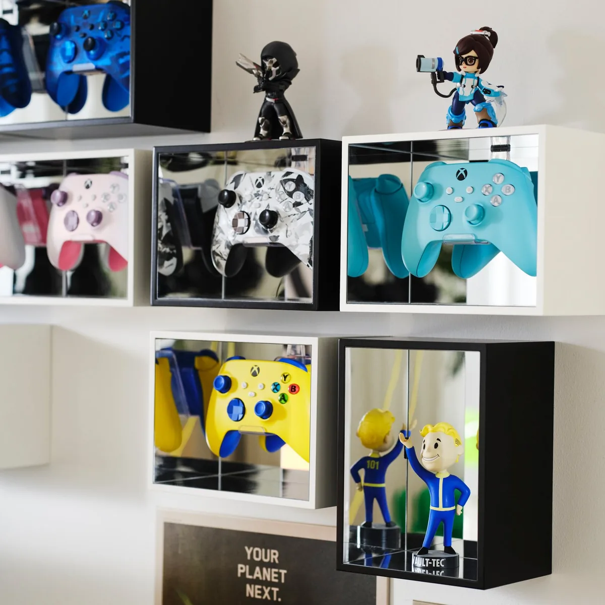 IKEA YXSTABY krabička na vystavení herního ovladače IKEA YXSTABY krabička na vystavení herního ovladače – bílé a černé vitríny se zrcadlovými stěnami a ovladači Xbox na zdi
