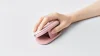 Logitech Pebble Up – růžová myš ve zvednutém režimu pod rukou na světlém stole