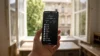 Telefon s Niagara Launcherem v ruce u okna, na obrazovce svisly seznam aplikaci