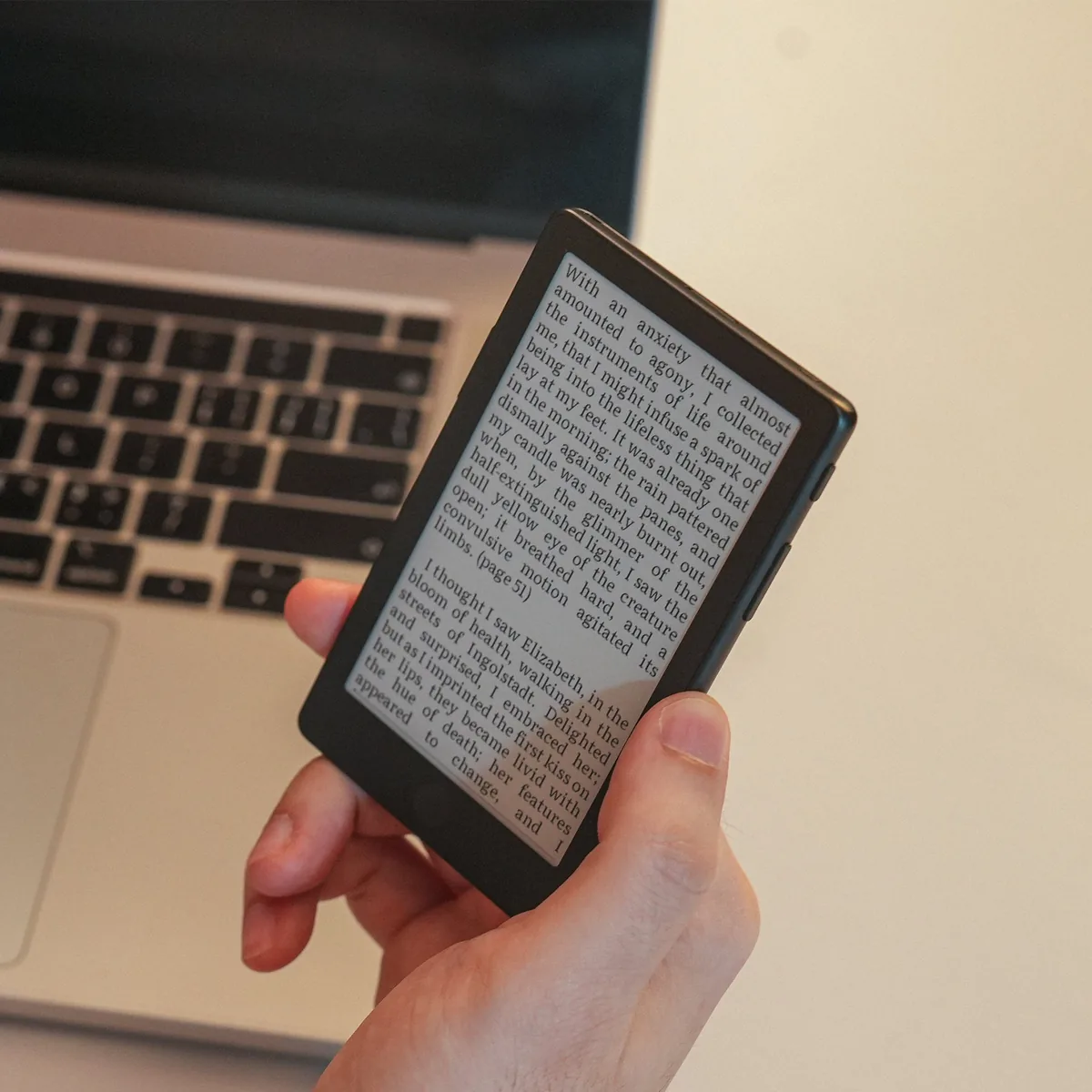 První recenze Xteink X4 Pro: kapesní čtečka rozdělila testery na dva tábory 1 Ruka drží kapesní čtečku Xteink X4 Pro s otevřenou knihou na displeji nad otevřeným notebookem