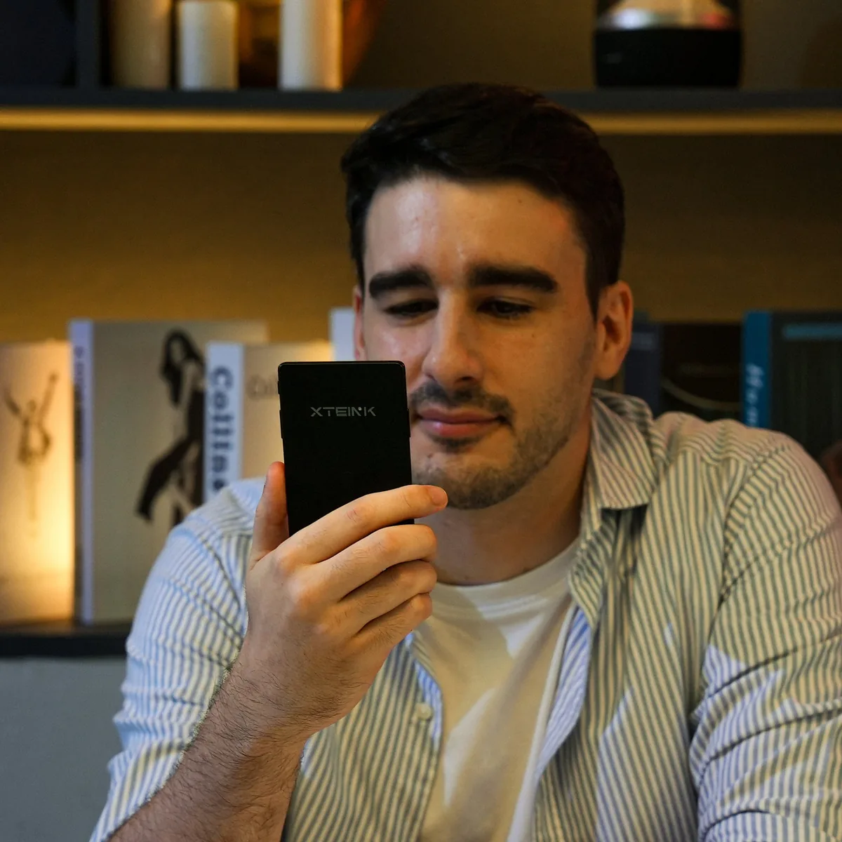 První recenze Xteink X4 Pro: kapesní čtečka rozdělila testery na dva tábory 3 Muž drží čtečku Xteink X4 Pro zadní stranou k objektivu před policí s knihami